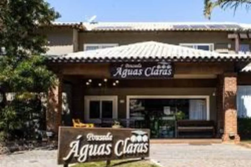 Fachada da Pousada Águas Claras: edifício de cor clara com detalhes em madeira e placa com o nome.