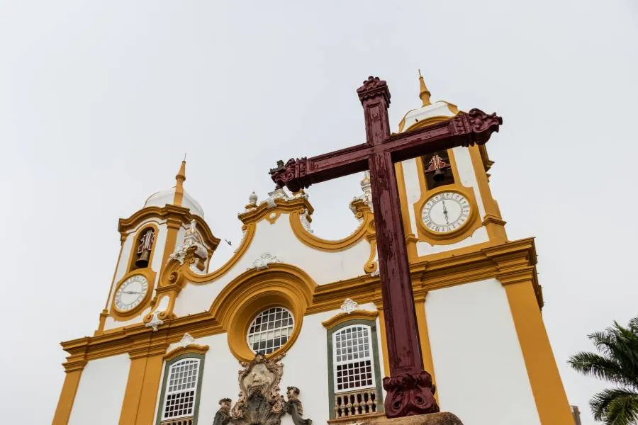 Imponente fachada barroca da Matriz de Santo Antônio em Tiradentes, Minas Gerais, com cruzeiro de madeira em primeiro plano.