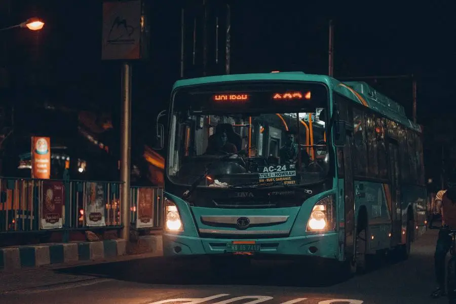 Um ônibus urbano de cor verde-água com as luzes acesas, parado em uma via noturna com sinalização de "STOP" visível no asfalto