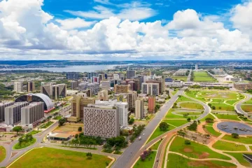 Vista aérea da cidade de Brasília com seus edifícios modernistas e o Lago Paranoá ao fundo.